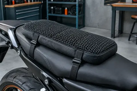 Coussin de selle moto noir à cellules en relief, posé sur une selle avec ses sangles visibles