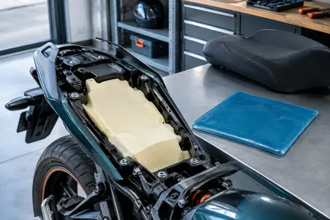 Coussin de selle moto AzulLanse en gel bleu posé près d’une selle dans un atelier soigné.