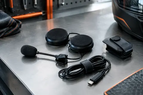 Kit audio moto noir avec haut-parleurs, microphone, clip de fixation et câble USB-C sur un établi