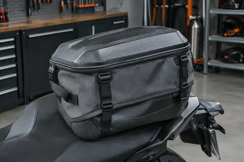 Sacoche de selle moto grise à coque ABS, posée sur une selle passager dans un atelier soigné.