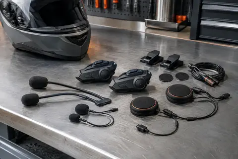 Kit intercom moto noir avec deux unités, haut-parleurs et microphones présenté sur un établi d’atelier.