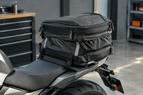 Sacoche de selle moto extensible avec sangles réfléchissantes, posée sur une moto dans un atelier sobre.
