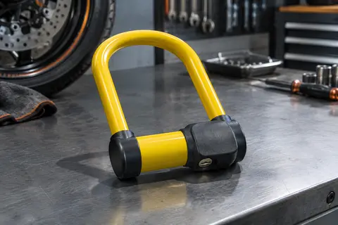Antivol moto en U Urban jaune avec fourche en acier trempé, présenté seul sur un établi d’atelier sobre.